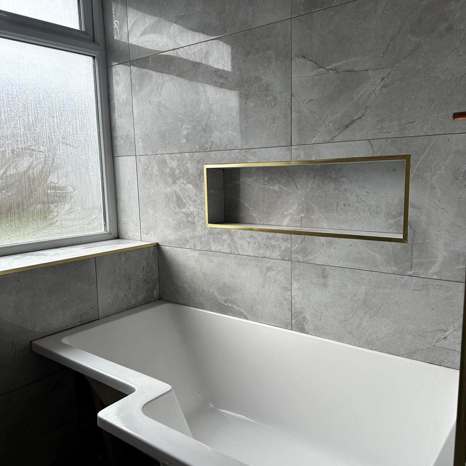 Luxury bathroom tiling — marble-effect porcelain with brass niche detail